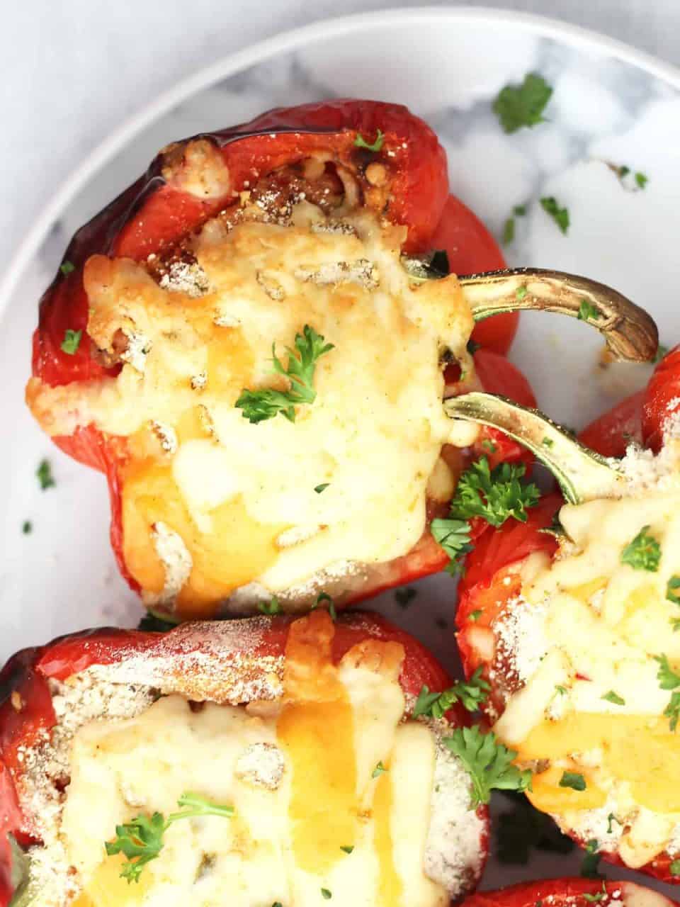 Three stuffed pepper halves topped with melted cheese on a serving plate.