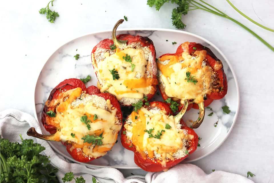 Four chicken parmesan stuffed peppers on a serving plate.