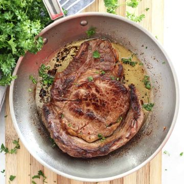 Beer marinated steak in a silver skillet garnished with fresh herbs.