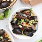 Chili mussels served in a white bowl and garnished with green onions.