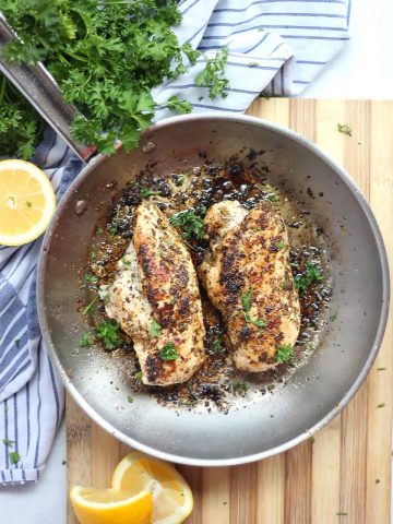 Two lemon oregano chicken breasts in a skillet garnished with fresh parsley.