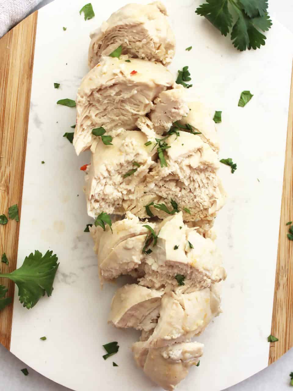 Sliced poached chicken on a chopping board.