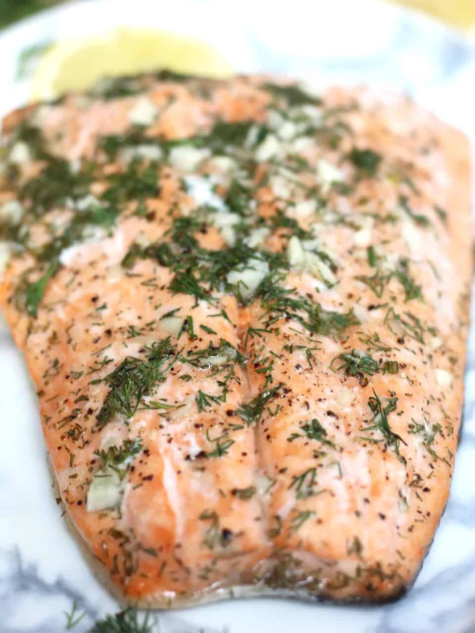 Honey lemon salmon fillet with dill and garlic on a serving plate.