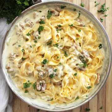 Pasta tossed in blue cheese sauce and walnuts in a skillet and garnished with fresh parsley.