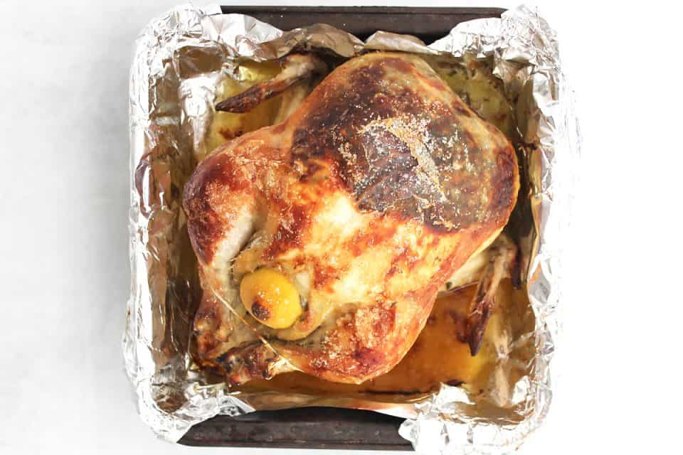 The roasted chicken in a foil lined baking tin.