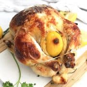 Buttermilk roasted chicken on a wooden chopping board next to fresh lemons and herbs.