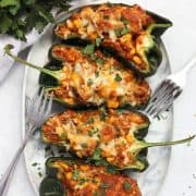 Chicken, cheese and corn stuffed poblano pepper halves on a white serving plate with two forks.