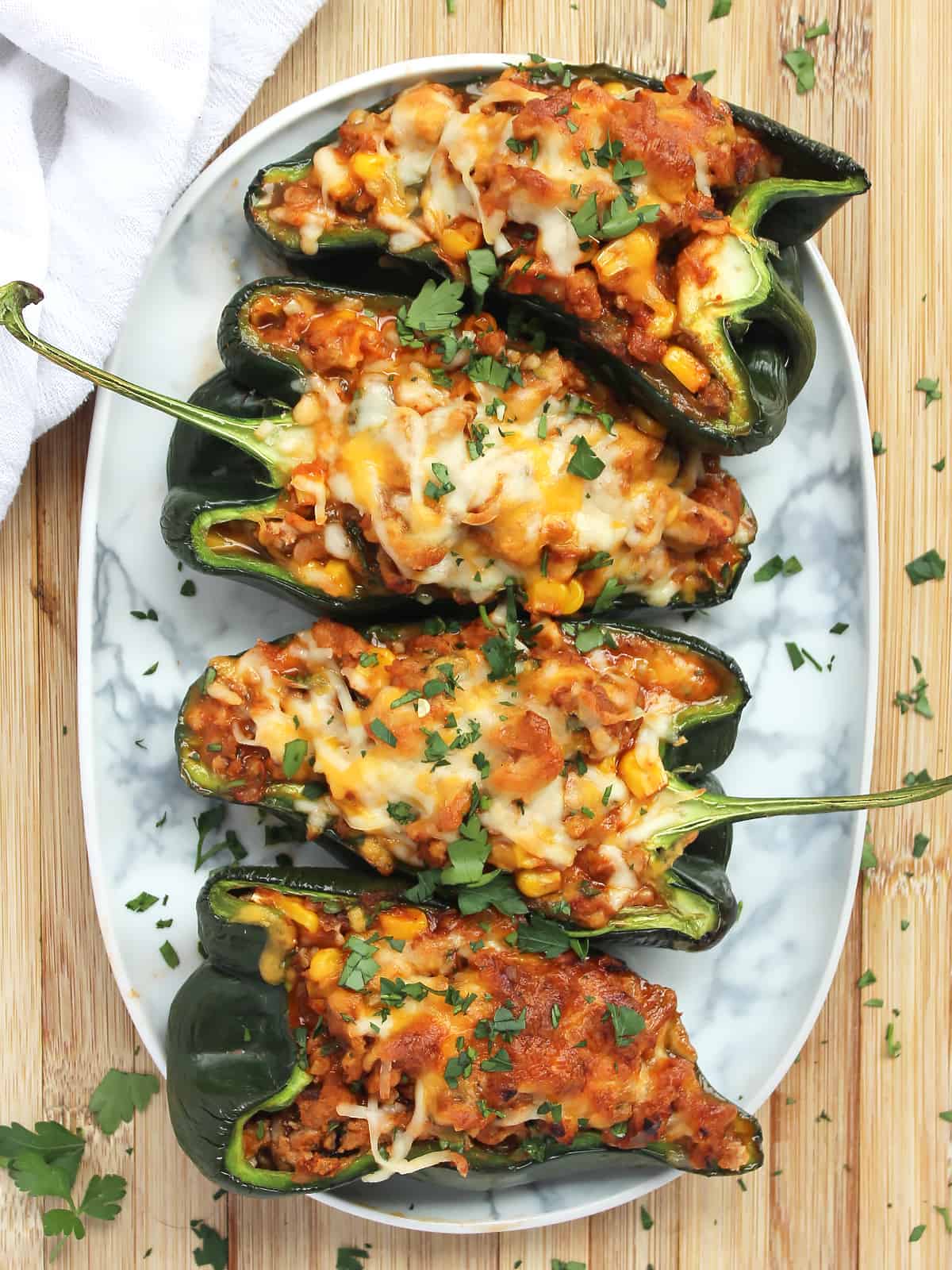 Stuffed poblano pappers on a serving plate on a wooden chopping board.