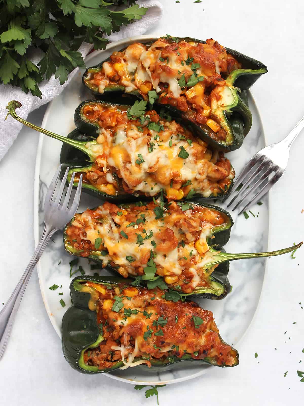 Four poblano pepper halves stuffed with chicken and corn and topped with cheese on an oval serving plate.