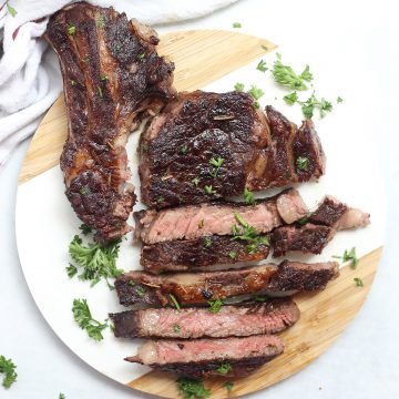Sliced red wine marinated steak on a round chopping board.