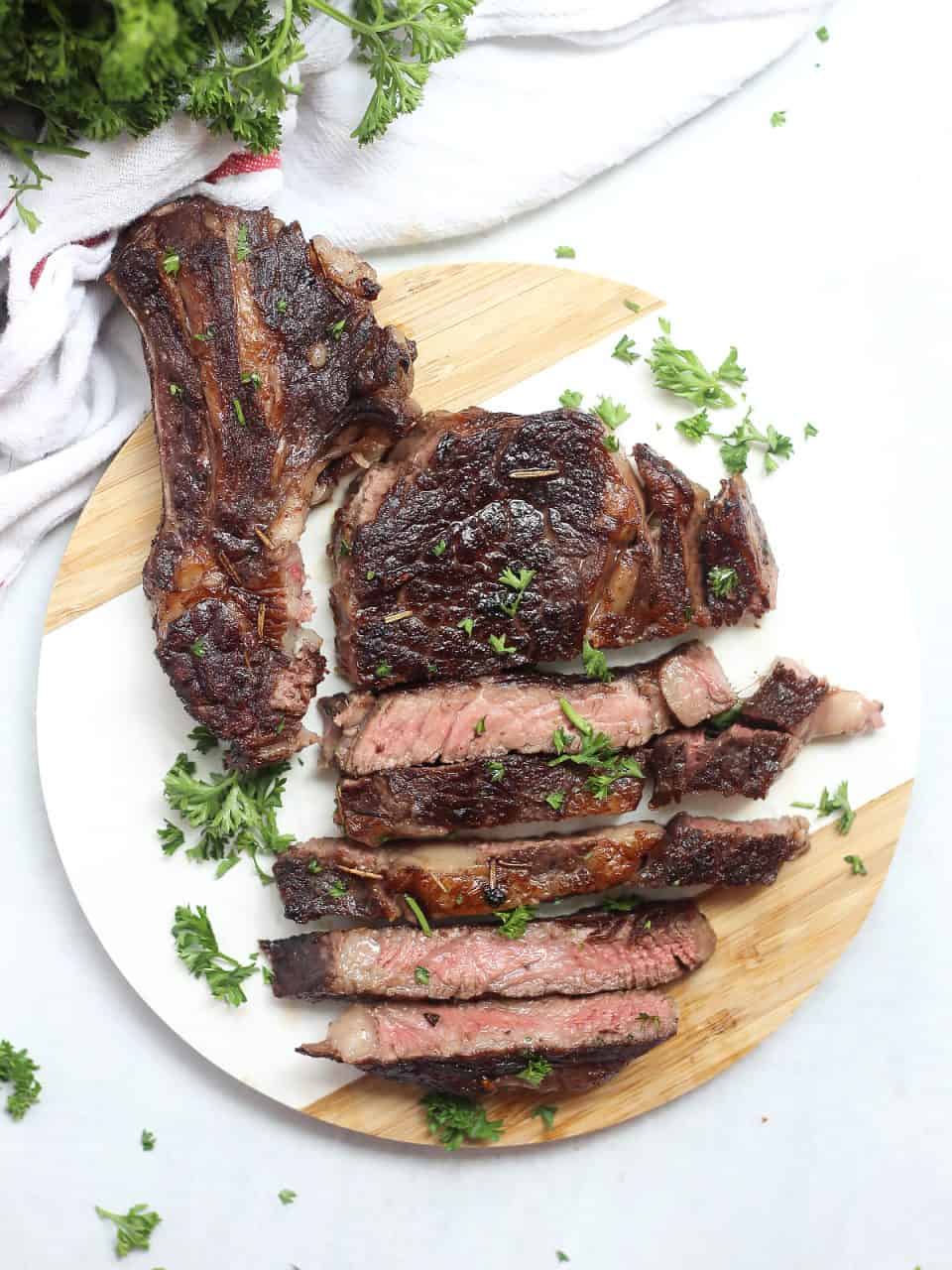 Sliced red wine marinated steak on a circular chopping board and garnished with fresh parsley.
