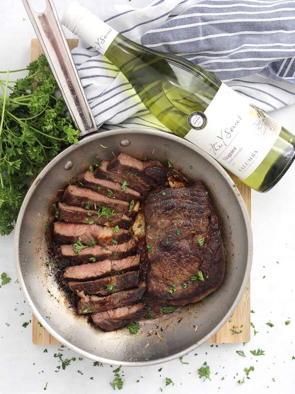 White wine marinated ribeye steaks in a skillet garnished with fresh herbs.