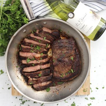 Two white wine marinated steaks in a skillet, one sliced into strips.