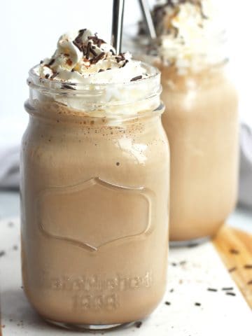 Two mason jars filled with chocolate coffee milkshake and topped with whipped cream.