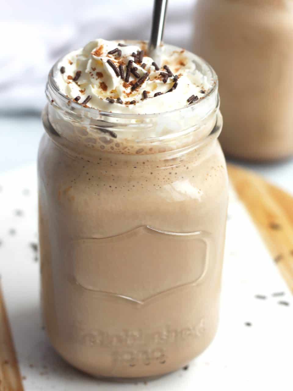 A milkshake in a mason jar topped with whipped cream and chocolate sprinkles.