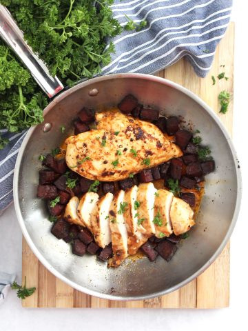 Two chicken breasts in a skillet with chorizo. One chicken breast is sliced into pieces.