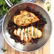 Two chicken breasts in a skillet with chorizo pieces.