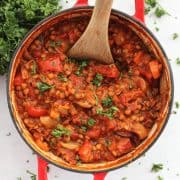 Roasted vegetable lentil bolognese in a red Dutch oven with a wooden spoon.