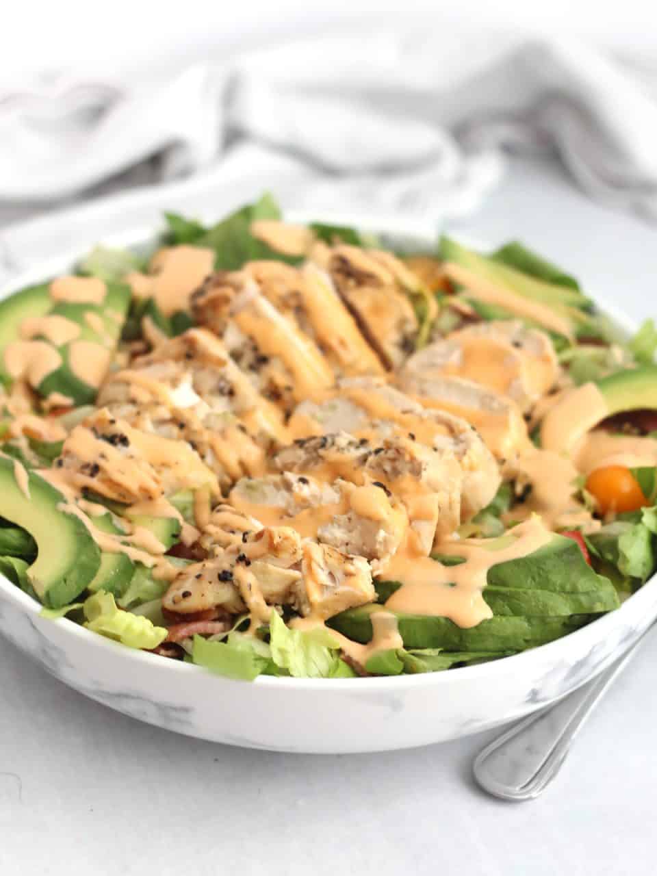 Sliced chicken breast drizzled with dressing on top of a bed of salad.