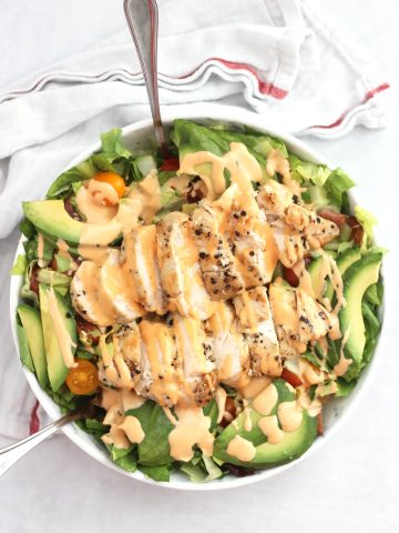 Overhead shot of a BLT chicken avocado salad in a bowl drizzled with a sauce.