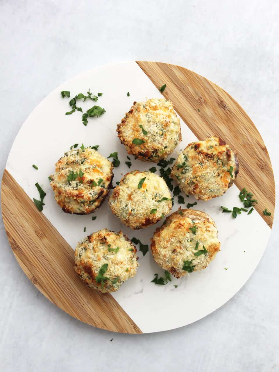 Overhead shot of six air fryer stuffed mushrooms on a circular chopping board and garnished with parsley.