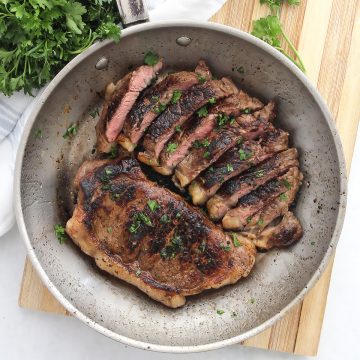 Two cola marinated steaks in a skillet. One sliced into pieces.