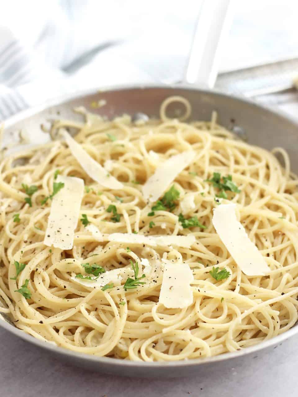 Spaghetti in a skillet topped with shaved parmesan and fresh parsley.