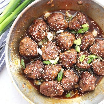 Honey sriracha meatballs in a skillet topped with sesame seeds and sliced green onion.