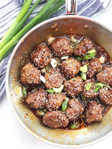 Overhead shot of the honey sriracha meatballs in a skillet next to fresh green onions.