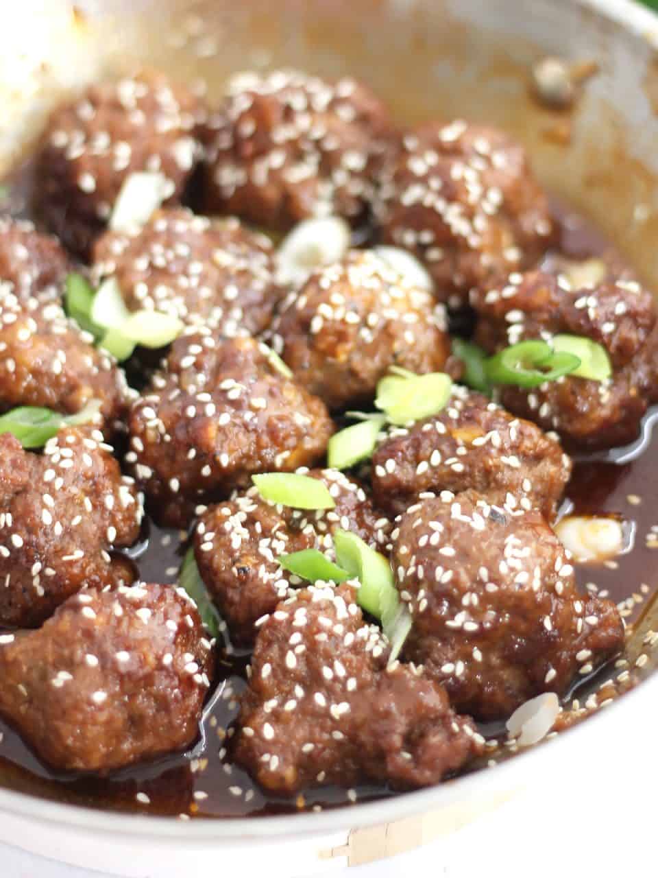 Close up of the cooked meatballs tossed in sauce in a skillet.