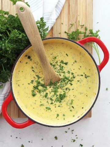 Overhead shot of creamy celery carrot soup in a red pot next to a bunch of fresh parsley.