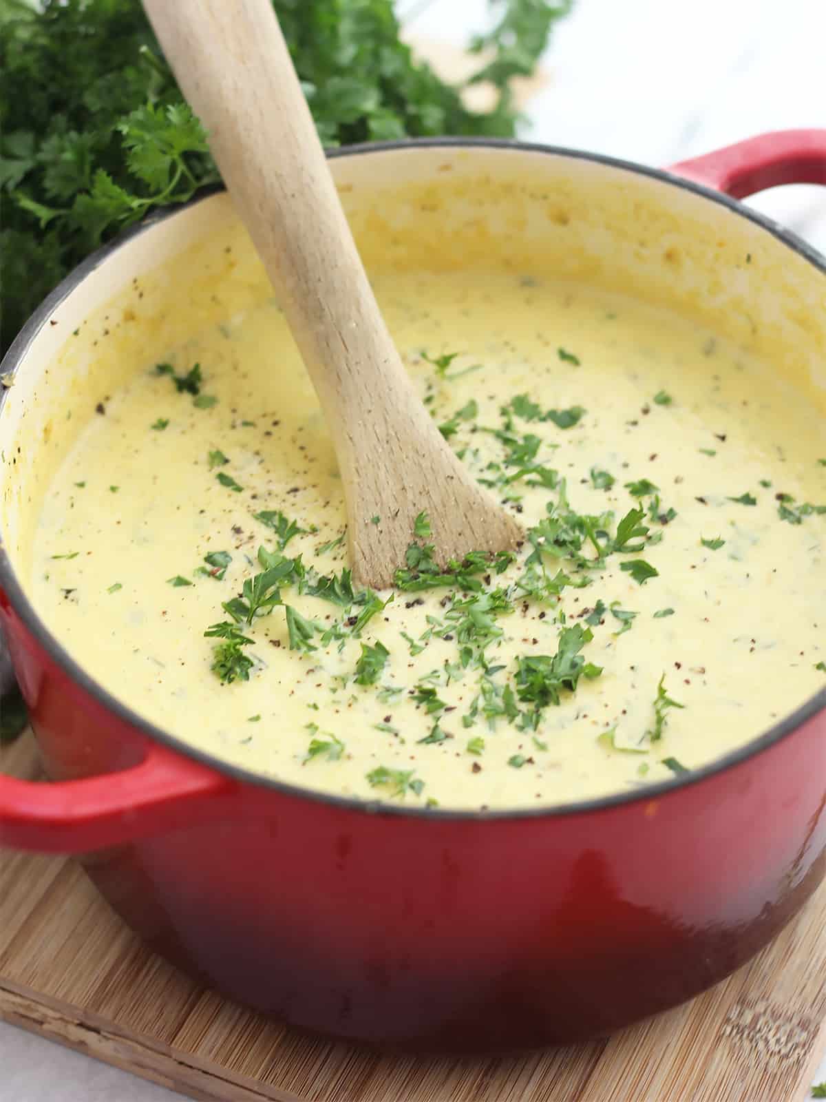 Celery carrot soup in a pot with a wooden spoon and garnished with fresh herbs.