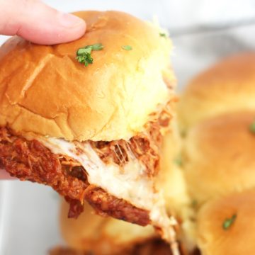 A hand holding a pulled pork slider with a cheese pull.
