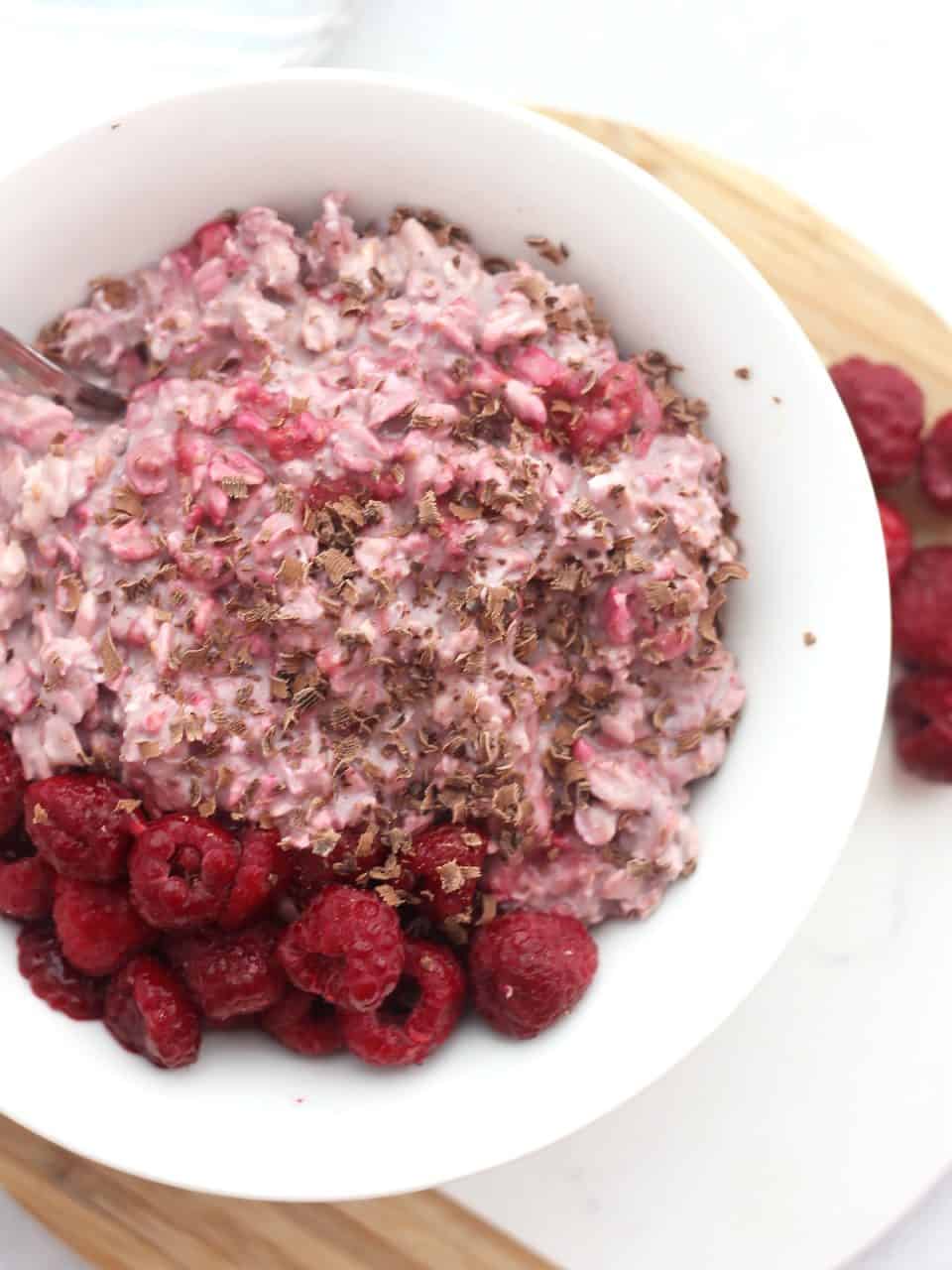 Overhead shot of a bowl of overnight oats topped with fresh raspberries and chocolate shavings.