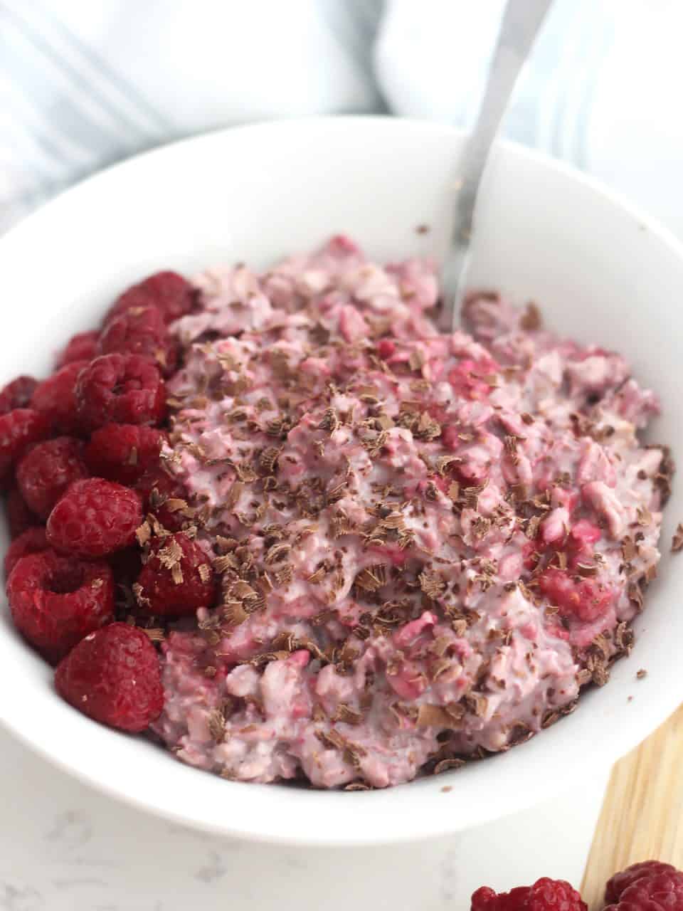 A spoon in a bowl of overnight oats with fresh raspberries.