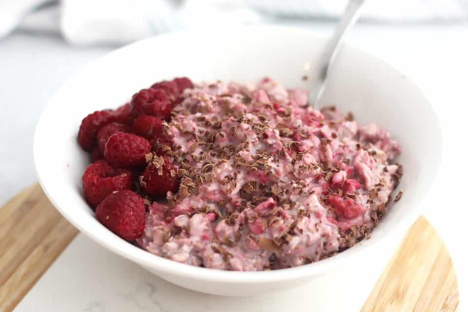 Close up of a bowl of raspberry overnight oats with a spoon in it.