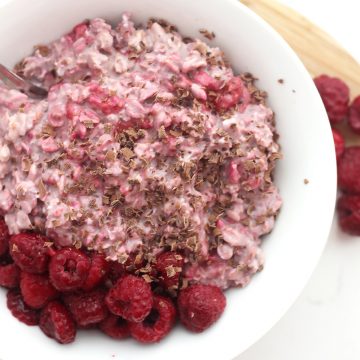 Overnight oats in a white bowl topped with fresh raspberries and grated chocolate.