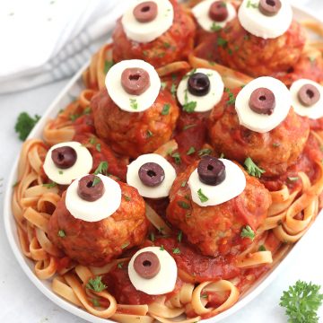 Halloween spaghetti and meatballs on a serving plate with fresh parsley garnish.