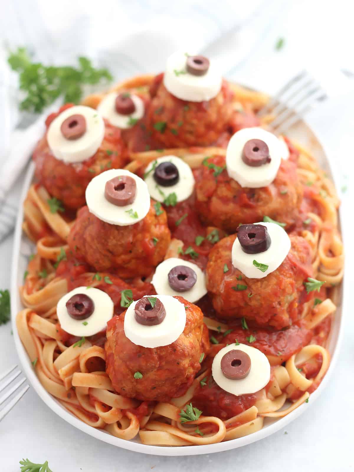 Six eyeball meatballs served on top of pasta and garnished with fresh herbs.
