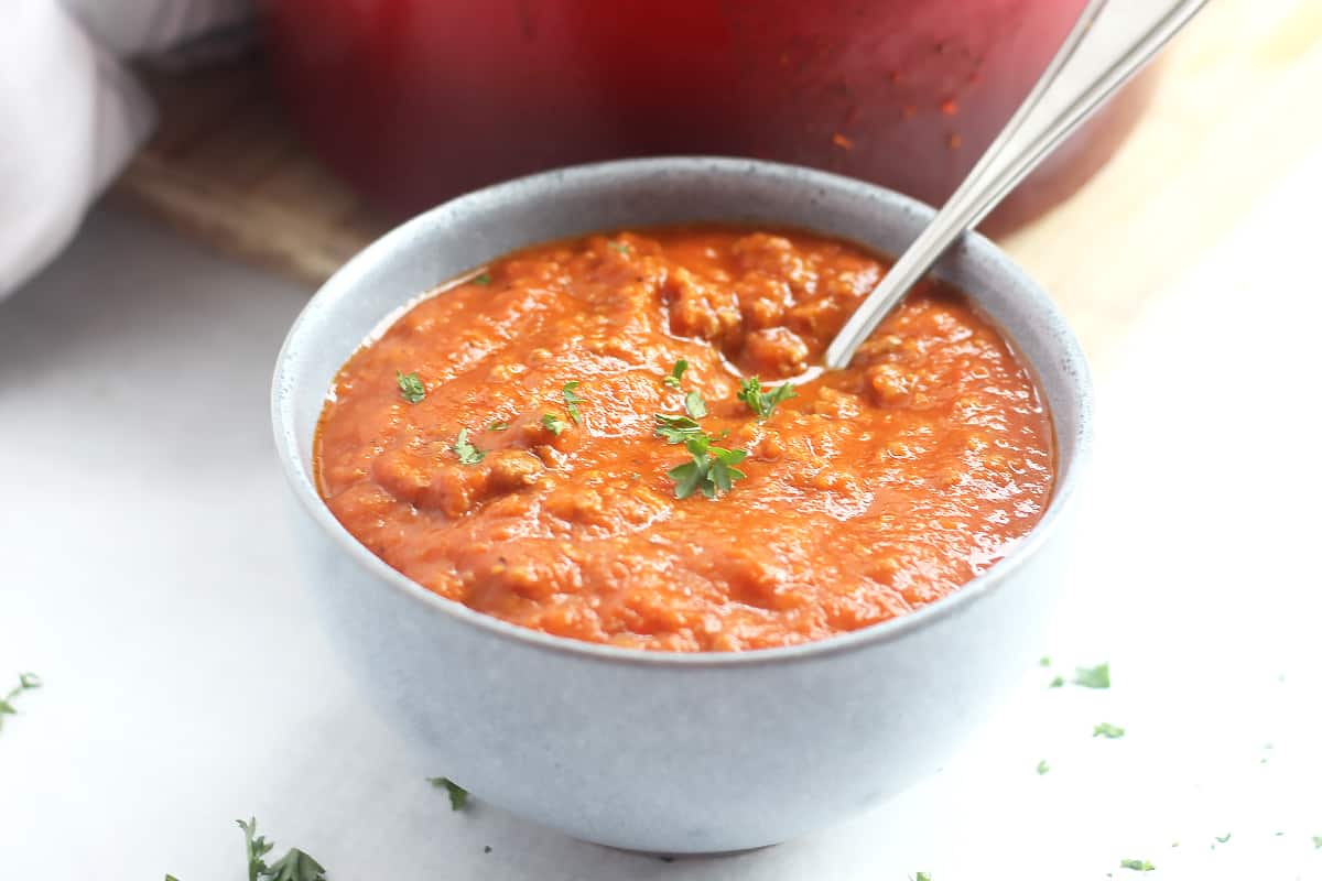 A bowl of beef and tomato soup garnished with fresh parsley.