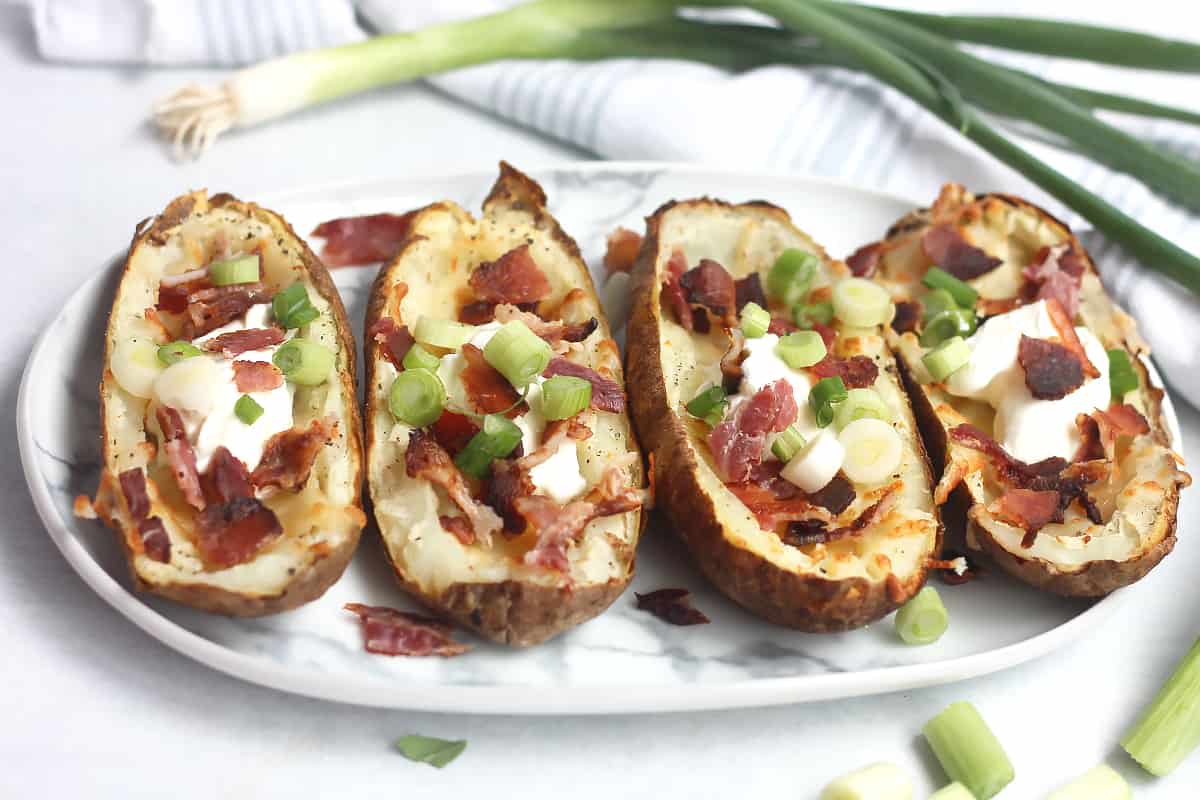 Four air fryer potato skins on a plate loaded with toppings.