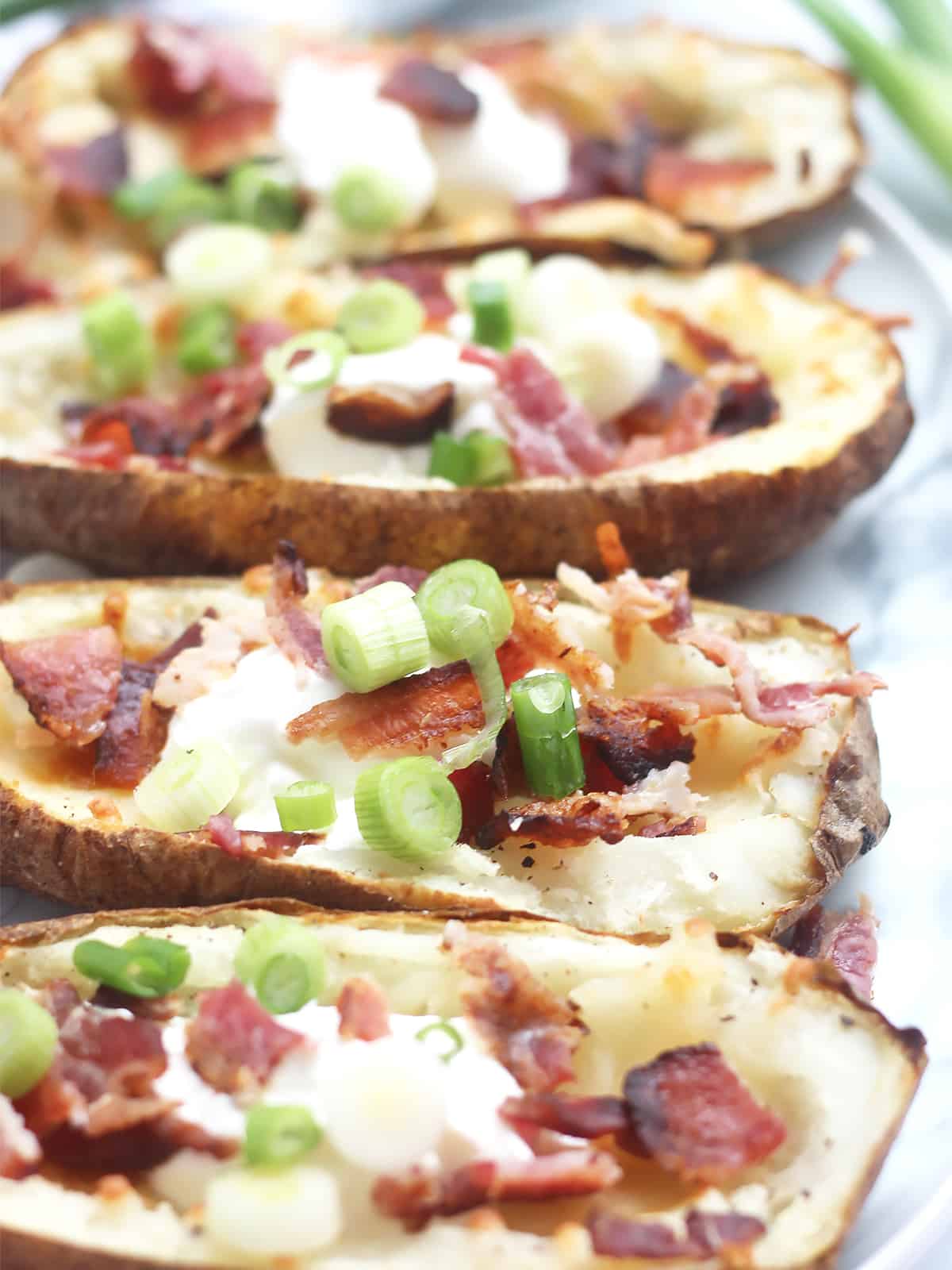 Close up of bacon, sour cream and green onions on top of the potato skins.