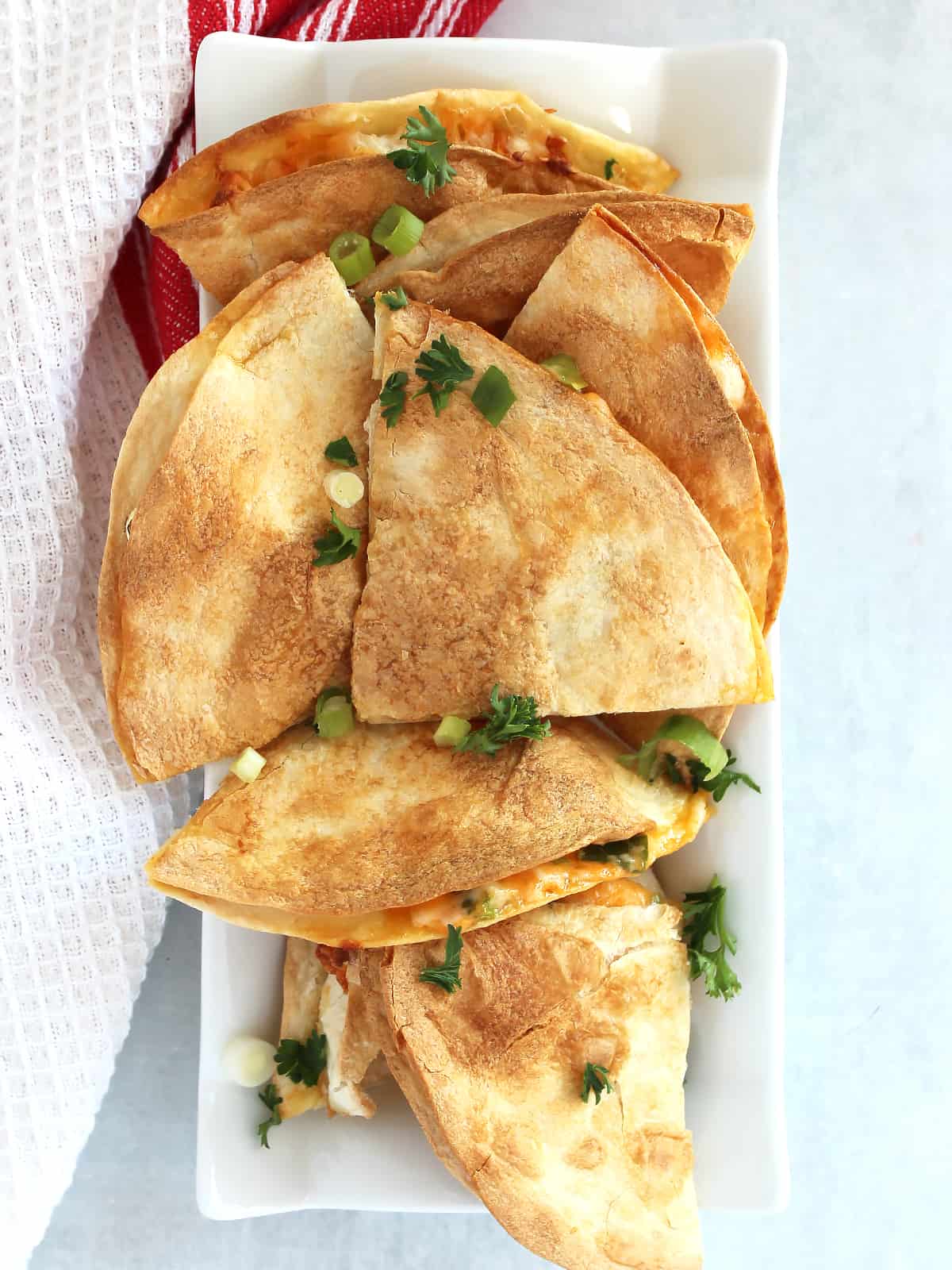 Overhead shot of air fryer cheese quesadillas on a serving plate, garnished with fresh parsley and green onions.