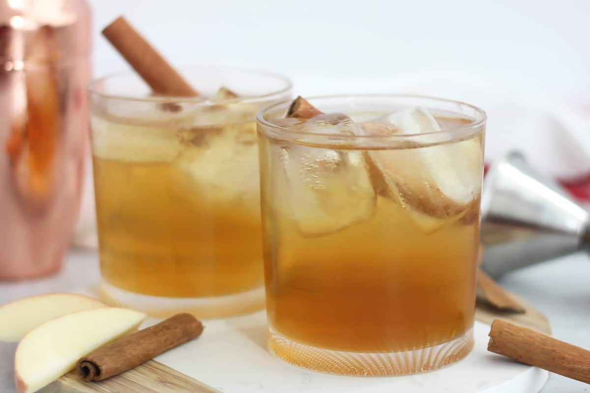 Two glasses of Fireball cocktail next to cinnamon sticks and apple slices.