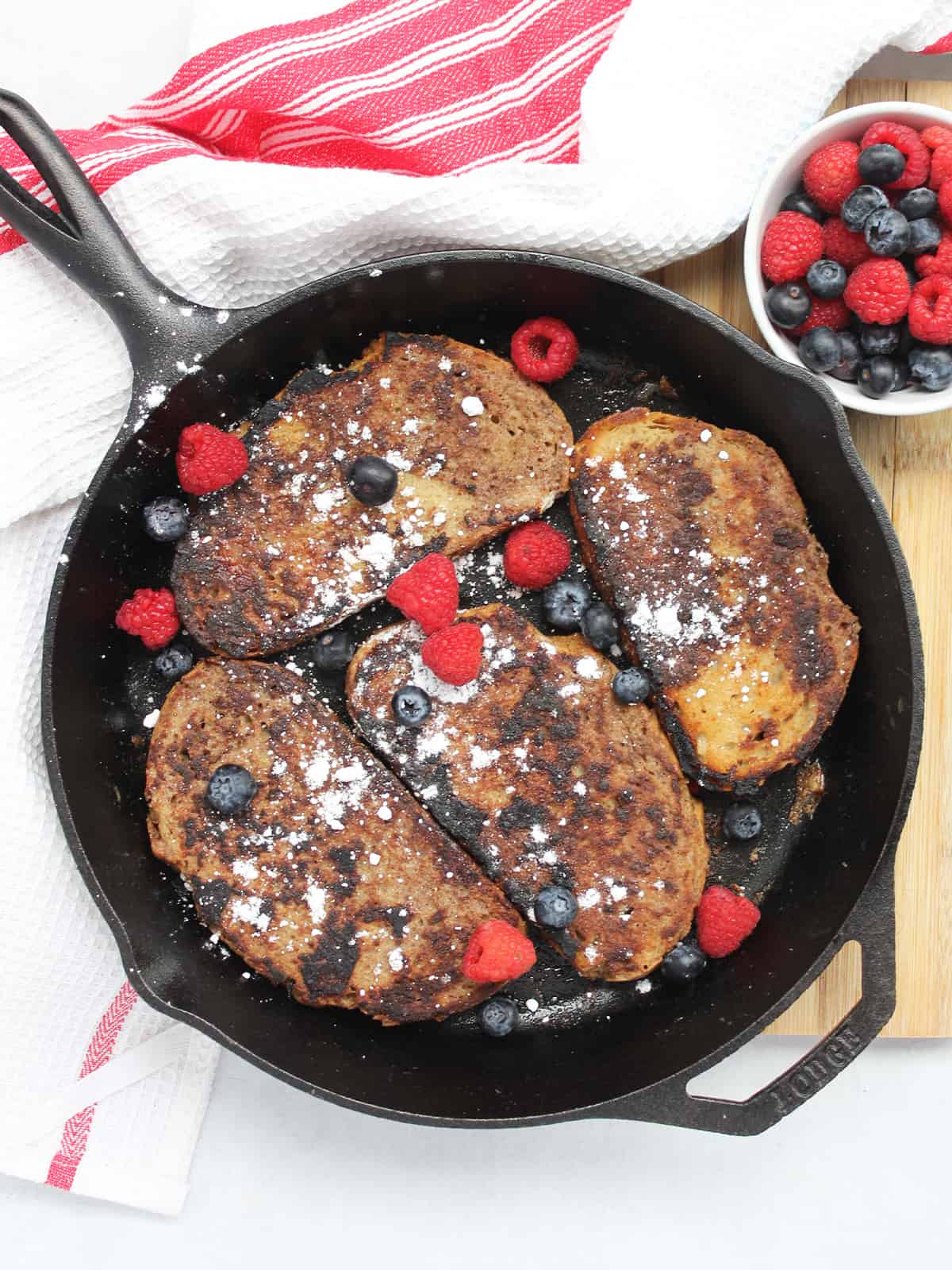 Four slices of pumpkin spice French toast in a cast iron skillet with powdered sugar and fresh berries.