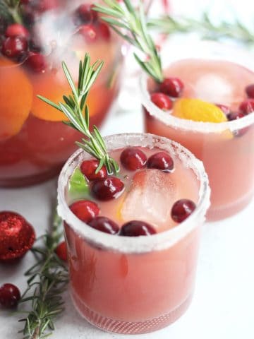 Two cranberry orange mocktails with fresh cranberries and sprigs of rosemary.