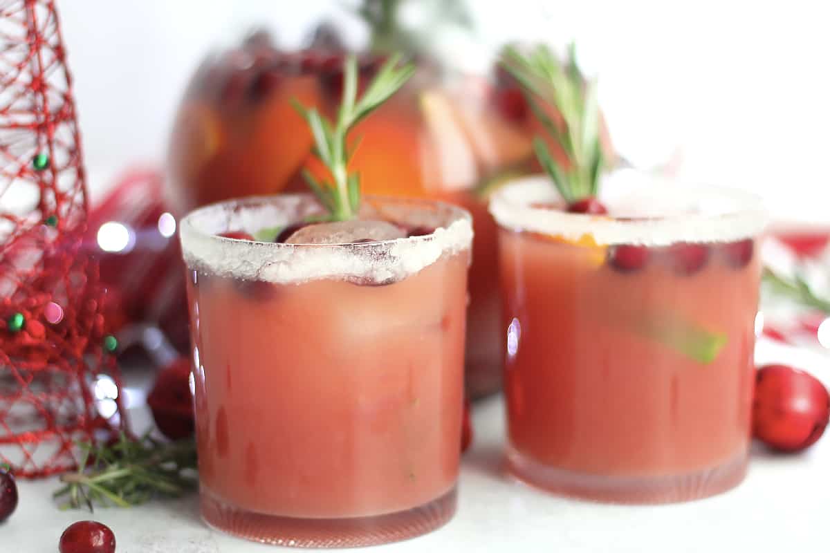 Two glasses of cranberry, orange and ginger mocktail garnished with rosemary.