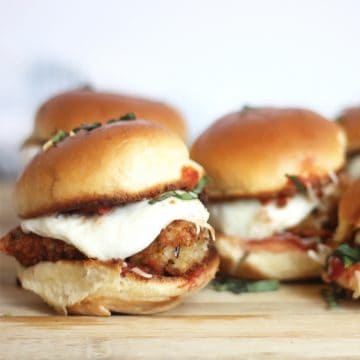 Three chicken parmesan sliders on a wooden chopping board.