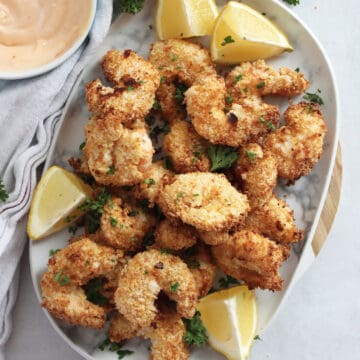 Air fried breaded shrimp on a plate with lemon wedges.