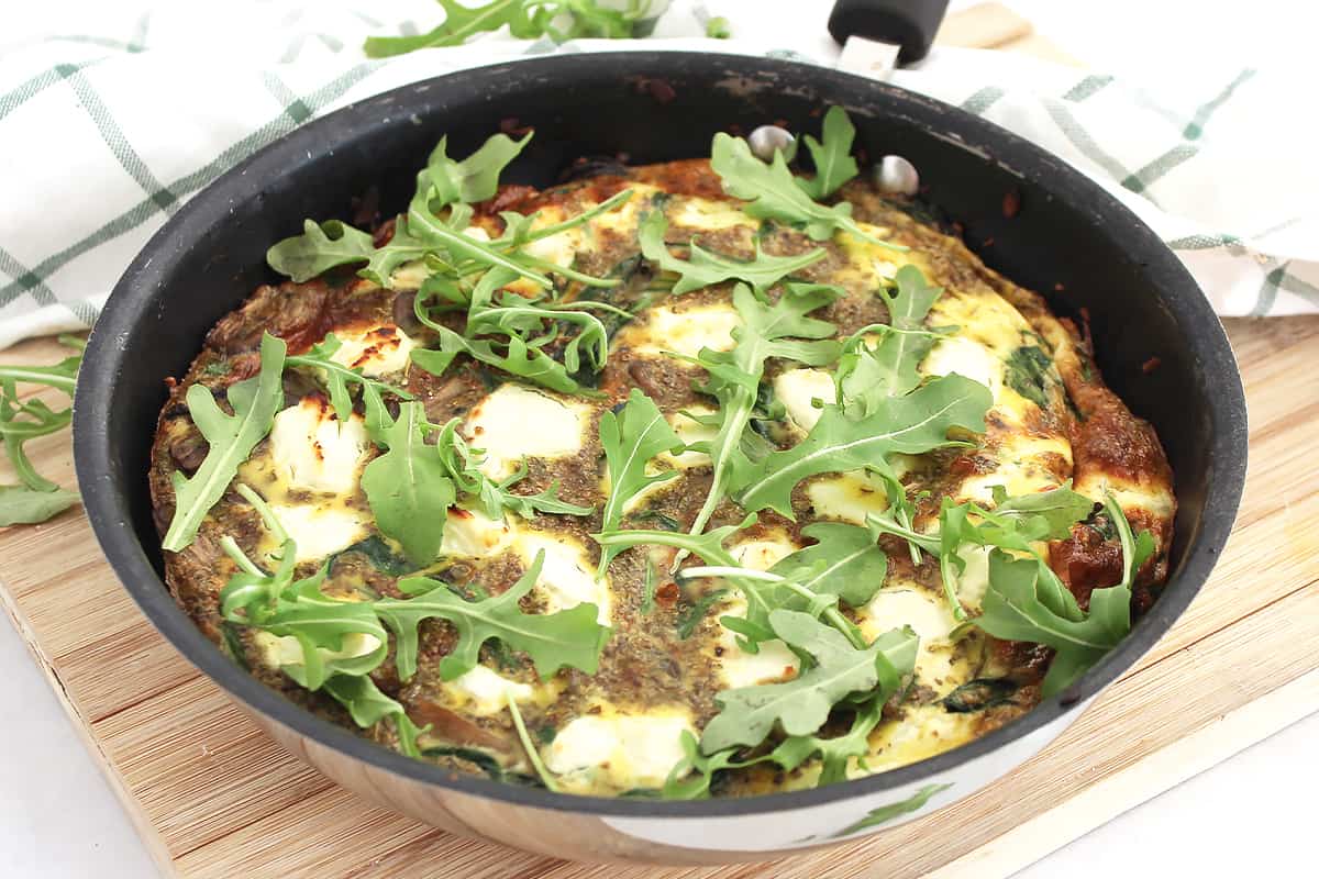 Goat cheese, mushroom and spinach frittata in a black skillet on a chopping board.